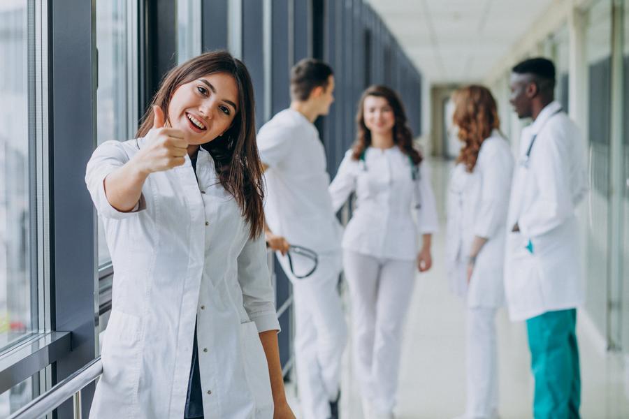 Une infirmière accompagnée de ses collçgues de travail fait un signe de 
    la main le pouce en l'air en guise de salut.