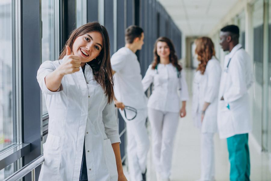 Une infirmière accompagnée de ses collçgues de travail fait un signe de 
    la main le pouce en l'air en guise de salut.